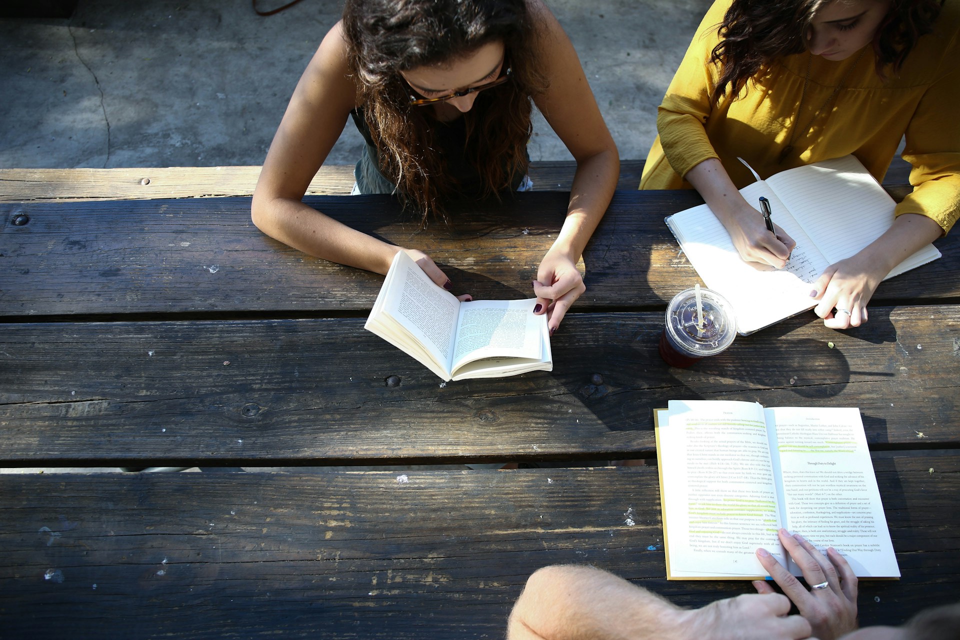 students at a picnic table outside school with books